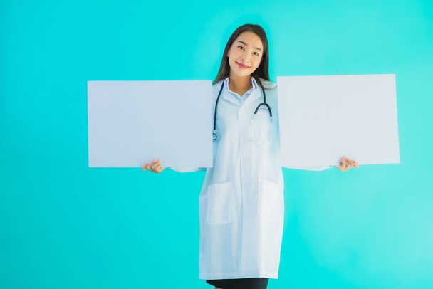 Portrait beautiful young asian doctor woman with empty card billboard banner on blue isolated background - Photo, Image