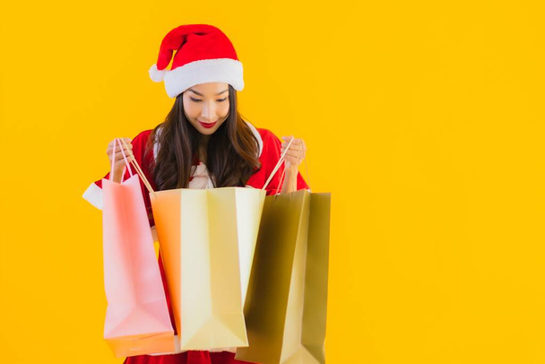 Portrait beautiful young asian woman wear christmas clothes hat with a lot of shopping bag on yellow isolated background - Φωτογραφία, εικόνα