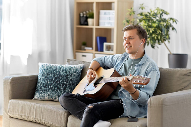 man with guitar, earphones and smartphone at home - Foto, afbeelding