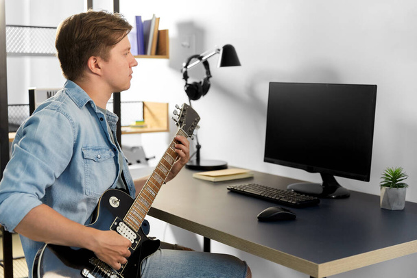 young man with computer playing guitar at home - Photo, image