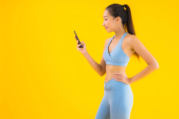 Portrait beautiful young asian woman wear sportwear with smart mobile phone on yellow isolated background - 写真・画像