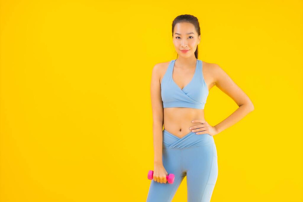 Portret mooie jonge aziatische vrouw met halter en sportschoenen klaar voor oefening op gele geïsoleerde achtergrond - Foto, afbeelding