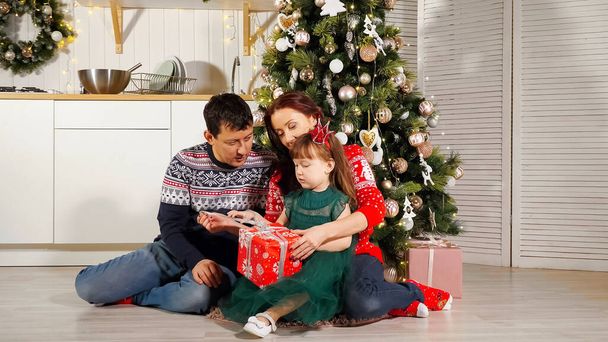 Mädchen packt Geschenkbox mit Eltern am Weihnachtsbaum aus - Foto, Bild