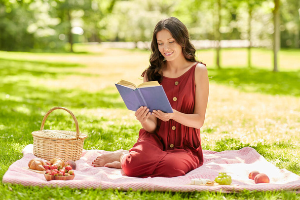 happy woman reading book at picnic in summer park - 写真・画像