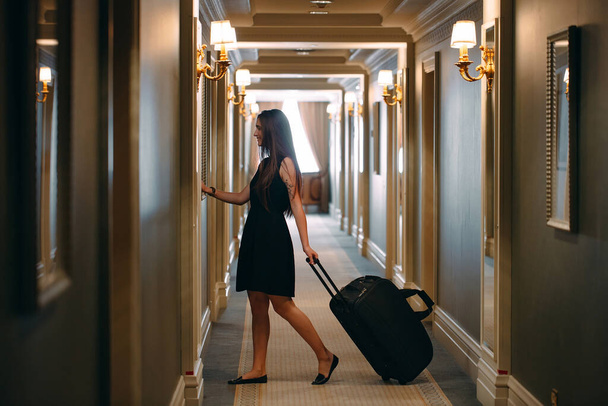 Young woman with handbag and suitcase in an elegant suit walks the hotel corridor to her room. - 写真・画像