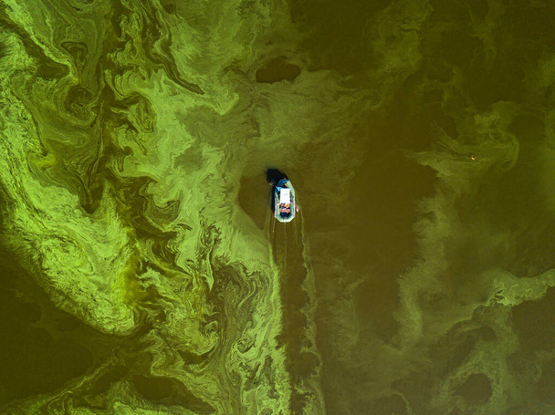 Fishing boat on green water, aerial drone view. Algae bloom in the river, green pattern on the water. - Photo, Image