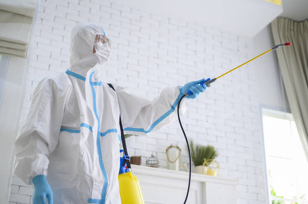 A medical staff in PPE suit is using disinfectant spray in living room, Covid-19 protection , disinfection concept . - Photo, Image