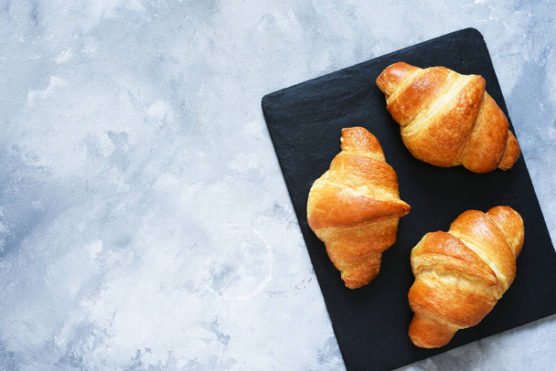 Croissants on a stone board on a concrete background. View from above. - Фото, зображення