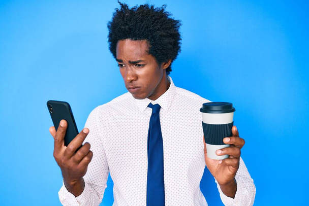 Handsome african american man with afro hair using smartphone and drinking a cup of coffee skeptic and nervous, frowning upset because of problem. negative person.  - Φωτογραφία, εικόνα