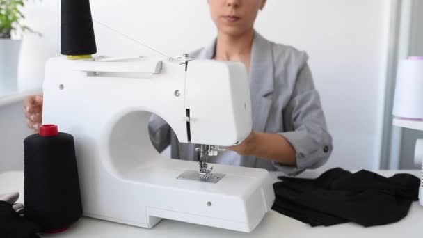 Mujer joven sastre está cosiendo en la máquina de coser en su mini taller. - Imágenes, Vídeo