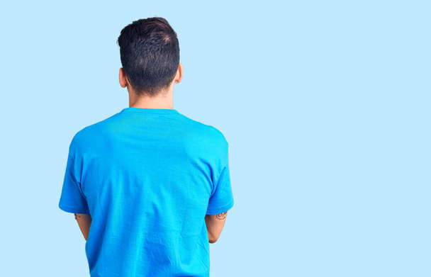 Νεαρός όμορφος άντρας με γενειάδα φορώντας ένα απλό μπλουζάκι που στέκεται πίσω κοιτώντας αλλού με σταυρωμένα τα χέρια  - Φωτογραφία, εικόνα