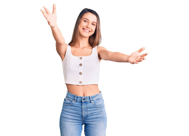 Young beautiful girl wearing casual sleeveless t shirt looking at the camera smiling with open arms for hug. cheerful expression embracing happiness.  - Photo, image