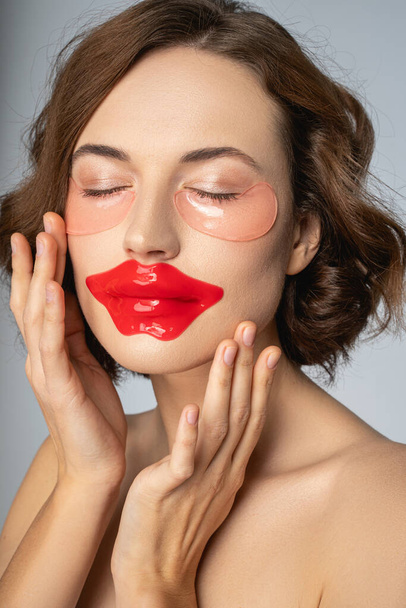Woman using a collagen lip mask and under-eye patches - 写真・画像