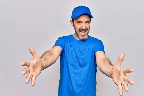 Middle age handsome deliveryman wearing cap standing over isolated white background looking at the camera smiling with open arms for hug. Cheerful expression embracing happiness. - Φωτογραφία, εικόνα