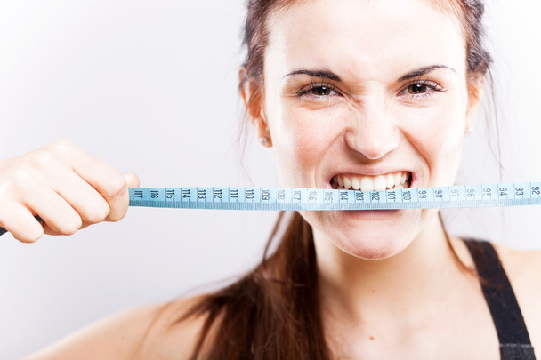 Angry young woman biting measuring tape - Foto, Bild