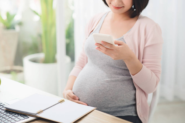 Abdomen girl working with smartphone at table in office in third trimester. Online working - Photo, Image