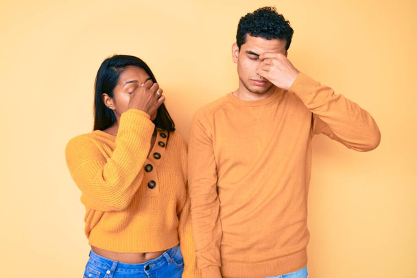 Beautiful latin young couple wearing casual clothes together tired rubbing nose and eyes feeling fatigue and headache. stress and frustration concept.  - Foto, Bild