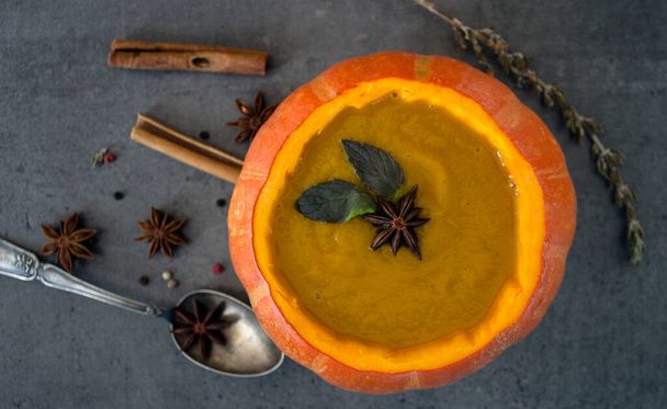 Squash soup in pumpkin bowl. Top view photo of pumpkin, apples, carrots anise stars and cinnamon sticks. Grey background. - Photo, Image