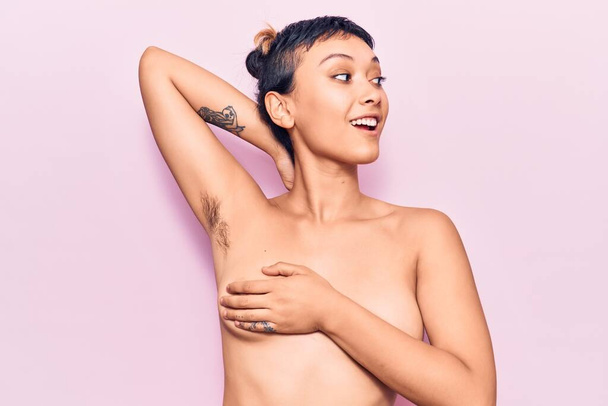 Young beautiful woman shirtless smiling happy. Standing with smile on face showing hairy armpit over isolated pink background - Photo, Image