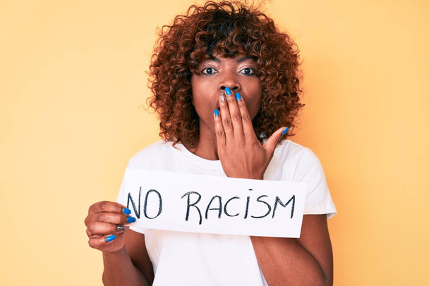 Joven mujer afroamericana sin pancarta de racismo cubriendo la boca con la mano, conmocionada y temerosa de equivocarse. expresión sorprendida  - Foto, imagen