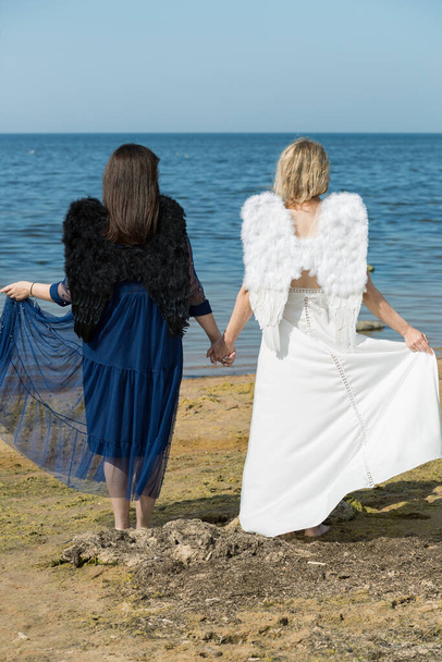 Město Saulkrasti, Lotyšsko. Dva andělé se chytají za ruce při chůzi podél mořského břehu.21.08.2020 - Fotografie, Obrázek
