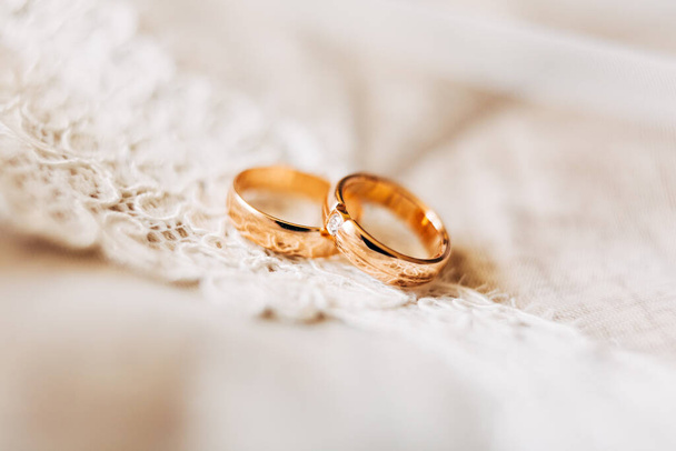 Zwei goldene Trauringe für Braut und Bräutigam mit Edelstein auf weißer Spitze. - Foto, Bild