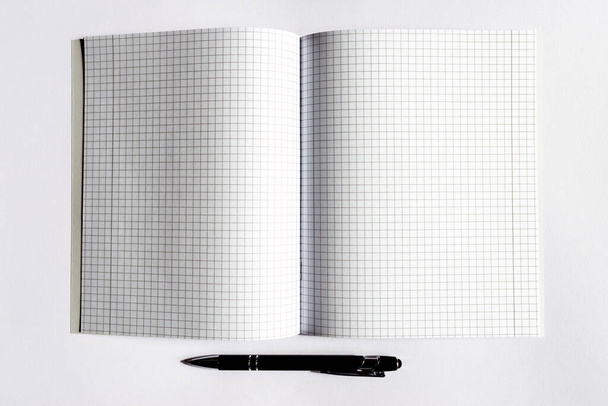 Kariertes Notizbuch mit schwarzem Stift auf weißem Hintergrund. Platz für Text.Leerzeichen kopieren.Banner-Werbung. - Foto, Bild