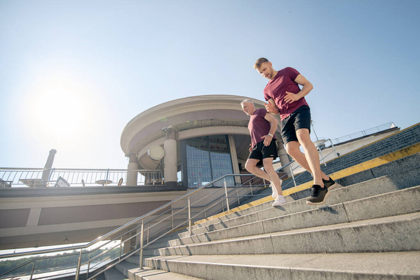 Young male and grey-haired male exercising, running down stairs - Foto, Imagem