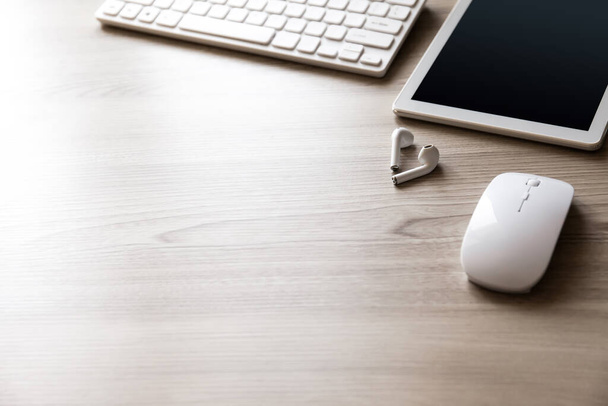 オフィスデスクフラット木製のテクスチャの背景にキーボード、マウス、タブレットPCやワイヤレスイヤフォンとビューをレイアウト. - 写真・画像
