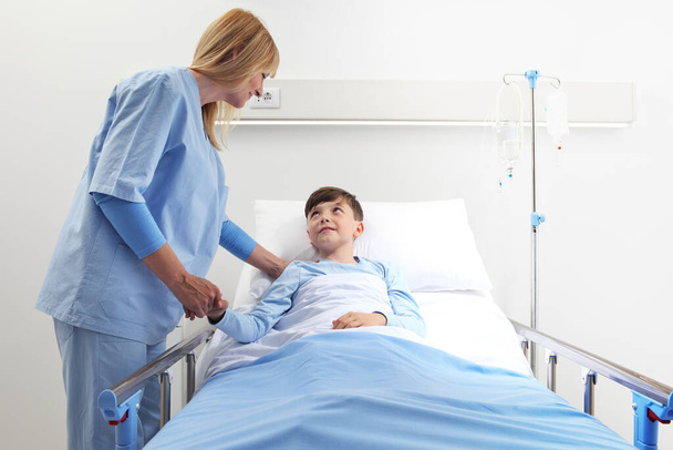 Little boy lying in hospital bed holding hands with smiling nurse - Foto, Imagem