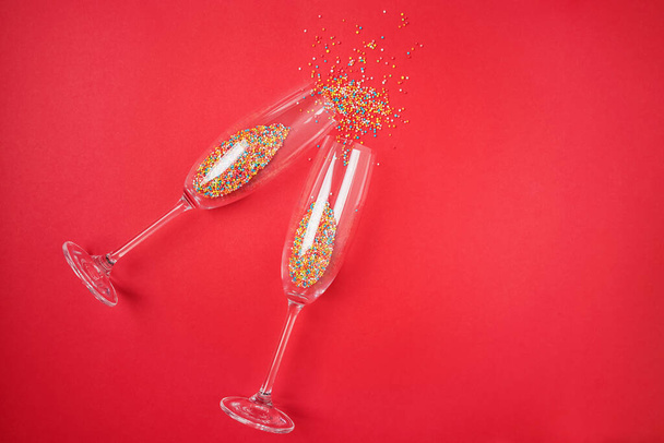 Champagne glass with colorful sugar sprinkles on red background. Holiday, party and celebration concept. Creative flat lay with copy space. - Фото, изображение