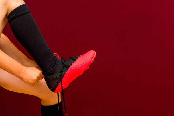 Fragment der Beine Junge kaukasische Fußballset Socken Fußballschuhe roten Hintergrund. Kopierraum. - Foto, Bild