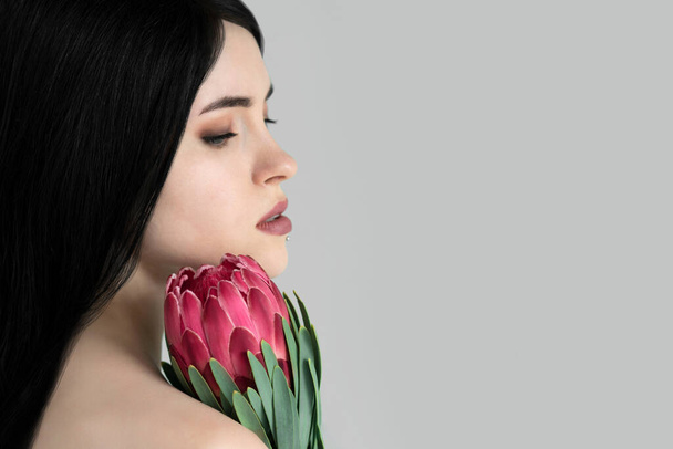 Portrait of a beautiful girl with dark hair and natural makeup with a protea flower in her hands. Fashion, beauty, makeup, personal care, hair, nature. - Fotografie, Obrázek