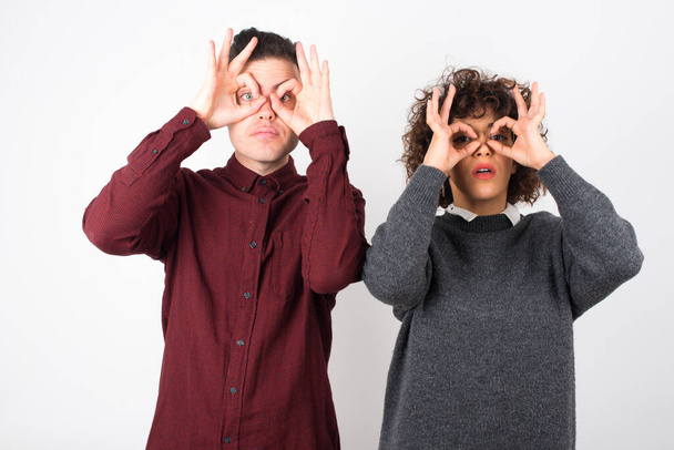  Paar, das Ok-Gesten mit beiden Händen zeigt, vorgibt, eine Brille zu tragen, erstaunt, etwas Erstaunliches zu sehen. Emotionen, Körpersprache und Gesten  - Foto, Bild