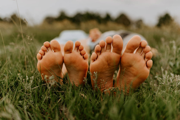 Nohy muže a ženy. Nohy chlapa a holku na trávě. Rodinný piknik v létě v parku na zelené neposekané trávě. - Fotografie, Obrázek