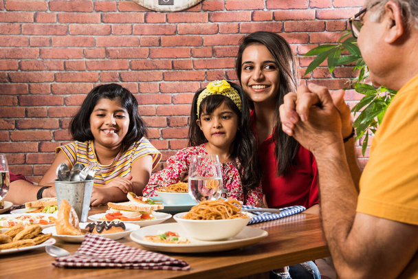 Familia india multigeneracional comiendo comida en la mesa de comedor en casa o restaurante. Abuelo, madre, padre y dos hijas del sur de Asia cenando juntos - Foto, Imagen