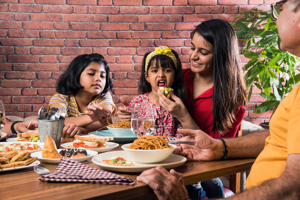 Indische Mehrgenerationenfamilie isst zu Hause oder im Restaurant am Esstisch. Südasiatischer Großvater, Mutter, Vater und zwei Töchter essen zusammen - Foto, Bild