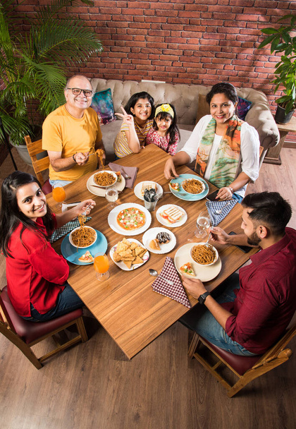Familia india multigeneracional comiendo comida en la mesa de comedor en casa o restaurante. Abuelo, madre, padre y dos hijas del sur de Asia cenando juntos - Foto, Imagen