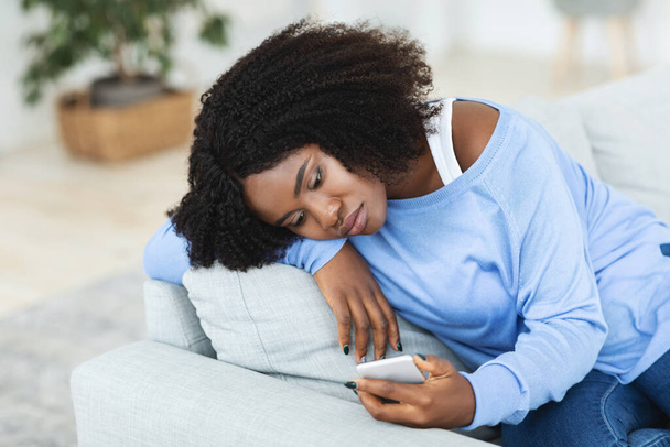 Разочарованная женщина проверяет мобильный телефон сидя на диване - Фото, изображение