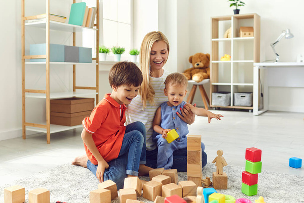 Mom and children are smiling playing with toys while sitting on the floor in the living room. Happy family - Фото, зображення