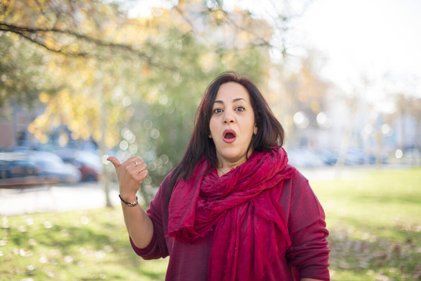 збентежена красива арабська жінка середнього віку, що показує щось у парку   - Фото, зображення