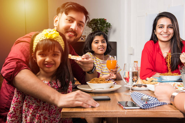 Indyjska wielopokoleniowa rodzina jedząca jedzenie przy stole w domu lub restauracji. Dziadek z Azji Południowej, matka, ojciec i dwie córki jedzą razem posiłek - Zdjęcie, obraz