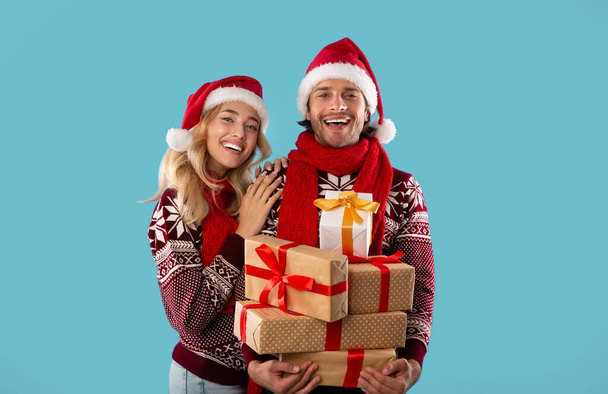 Porträt eines entzückenden jungen Paares in Weihnachtskostümen mit einem Haufen Geschenkschachteln auf blauem Hintergrund - Foto, Bild