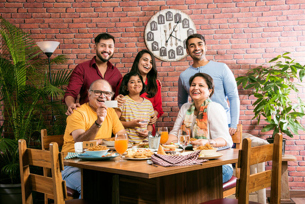 Familia india multigeneracional comiendo comida en la mesa de comedor en casa o restaurante. Abuelo, madre, padre y dos hijas del sur de Asia cenando juntos - Foto, imagen