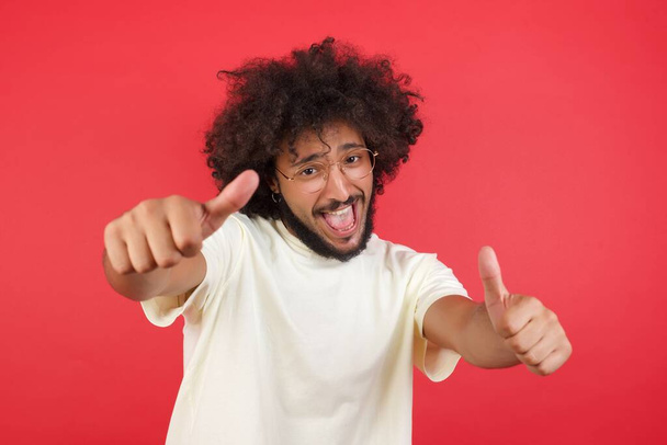 Młody człowiek z afro włosy z kciukami do góry na czerwonej ścianie  - Zdjęcie, obraz
