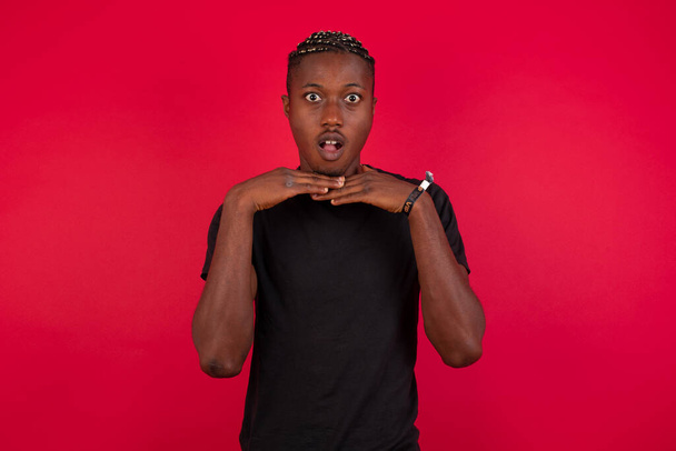African American man wearing black t-shirt over red background touching chin with hands having good time. - Fotoğraf, Görsel