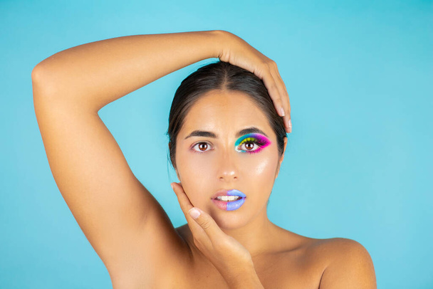 Schoonheidsportret van vrouwelijk model met levendige make-up aan de ene kant van het gezicht en schoon gezicht aan de andere kant op blauwe achtergrond en blauwe lippen. - Foto, afbeelding