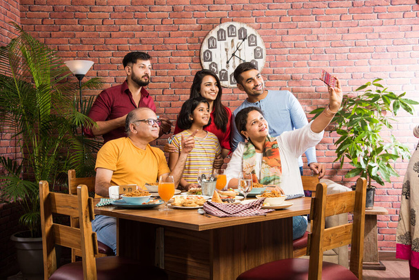 Indický multigenerační Rodina jíst jídlo u jídelního stolu doma nebo v restauraci. Jihoasijský dědeček, matka, otec a dvě dcery spolu povečeřeli - Fotografie, Obrázek