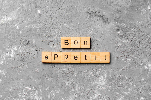 Bon Appetit słowo napisane na bloku drewna. Bon Appetit tekst na stole cementowym do projektowania, koncepcja. - Zdjęcie, obraz