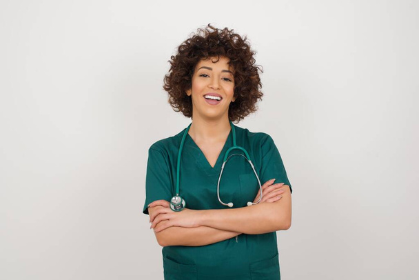 Mooie jonge doktersvrouw in medisch uniform met vrolijk gezicht glimlachend met gekruiste armen vol zelfvertrouwen naar de camera kijkend. Positief persoon. - Foto, afbeelding
